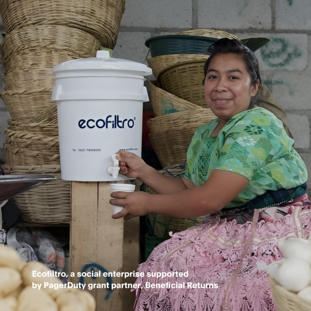 Seated woman smiling while pouring water into a cup from a water filter with the words “ecofiltro” written on the bucket.
