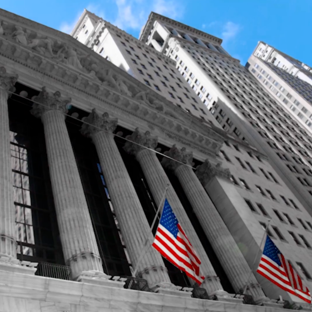 Facade of the New York Stock Exchange with American flags waving under a blue sky